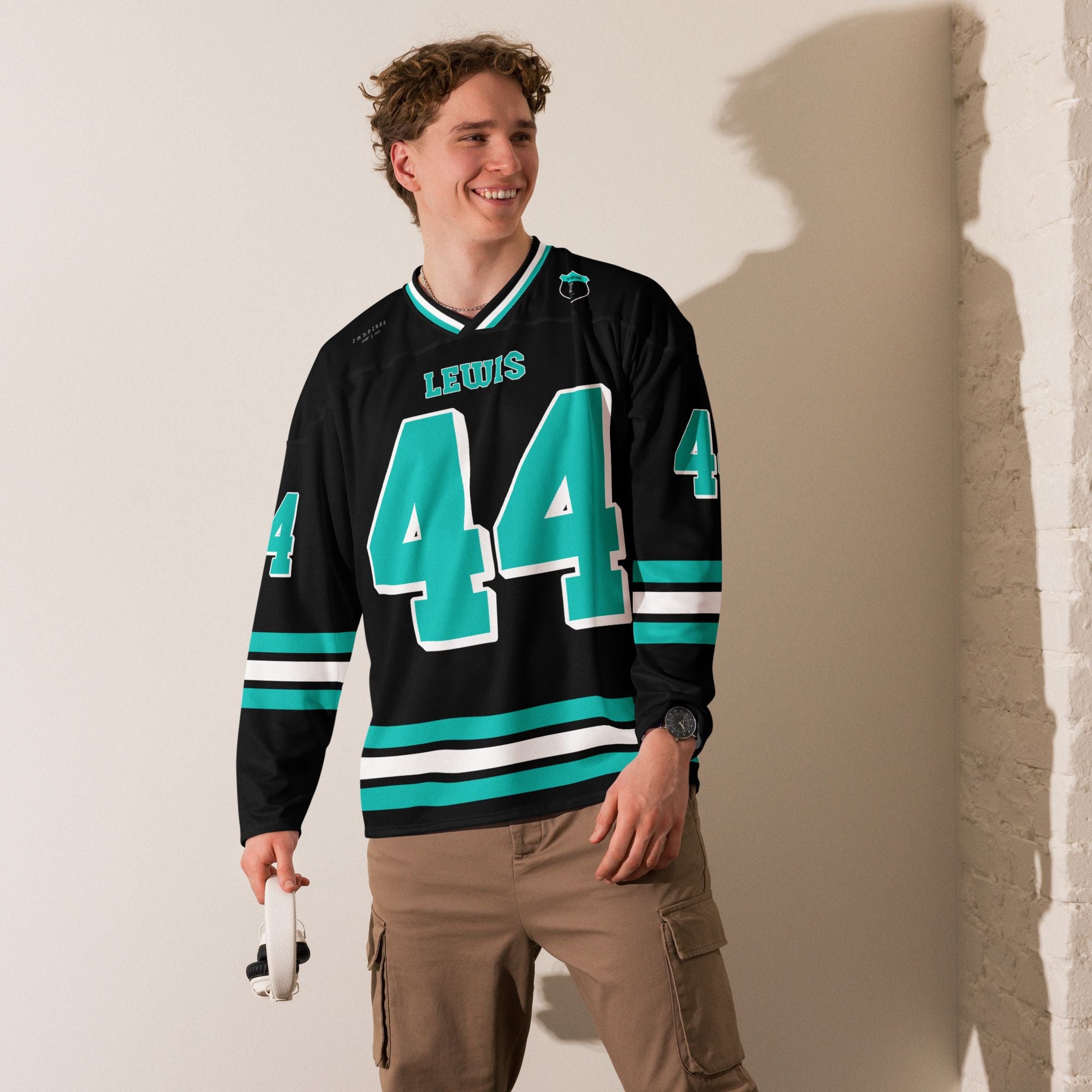 A black hockey jersey with three stipes on the bottom the middle one is white and the bottom and top are highligh blue / green. It has the number 44 that Lewis Hamilton races with in F1 that is filled with highlight blue/green and a white outline, it is displayed on the back and front. Also there is text on the front and back "Lewis"
